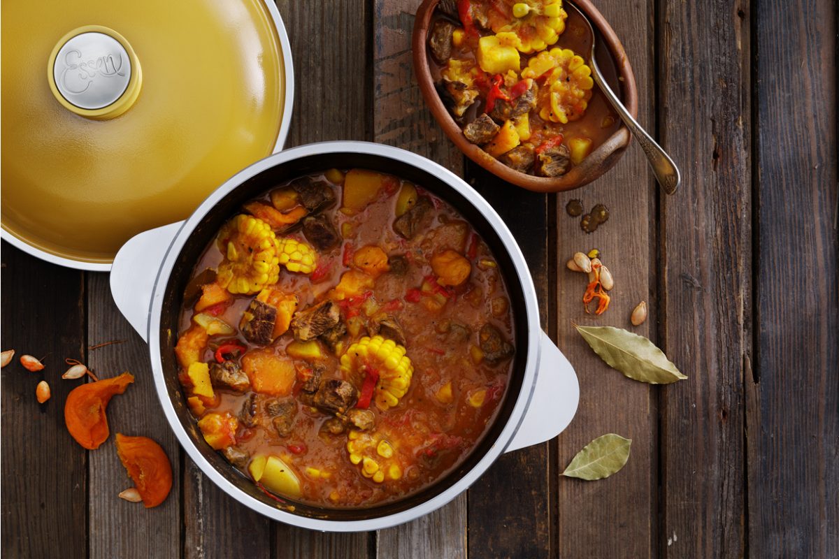 Una olla de locro criollo tradicional, un guiso espeso con carne, maíz y zapallo, listo para servir en una mesa de madera.