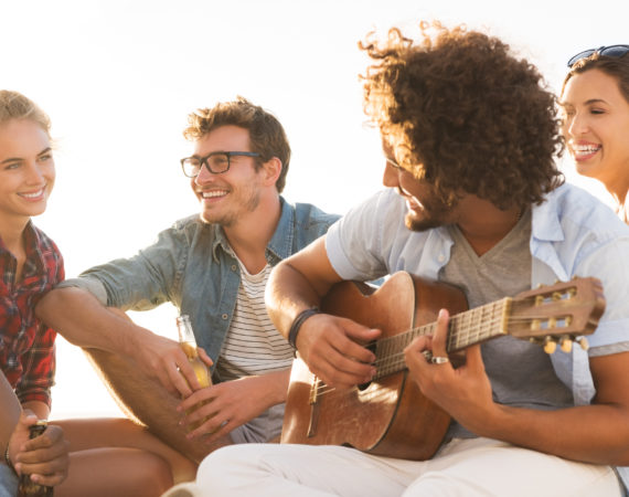 Grupo de amigos en la playa tocando la guitarra y disfrutando del encuentro