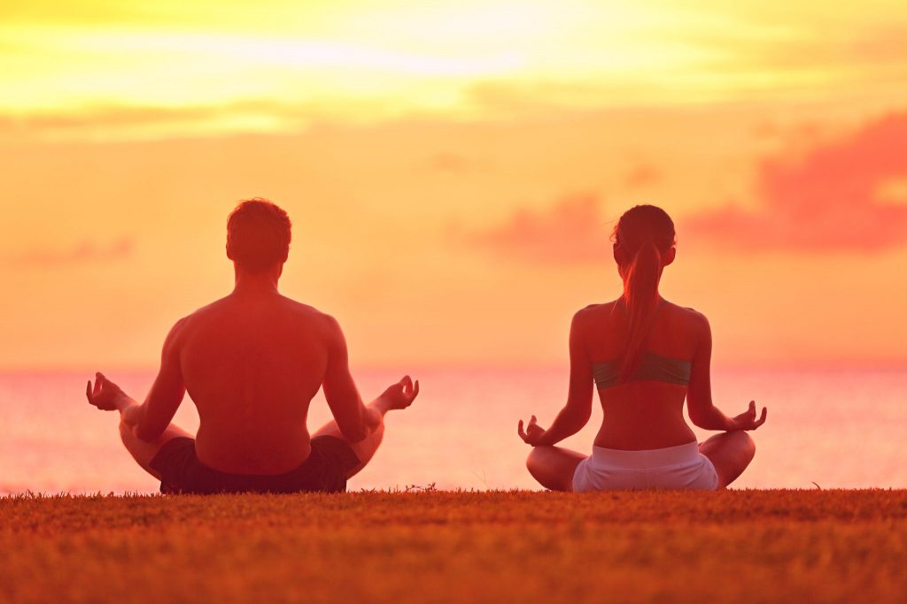 Pareja practicando meditación mindfulness al atardecer como herramienta para encontrar fortaleza y paz interior en momentos de dolor.