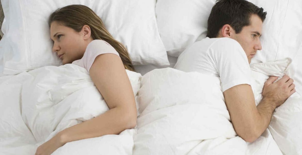 Mujer y hombre pensativos, acostados en la cama, simbolizando falta de deseo sexual