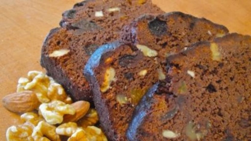 Primer plano de varias rebanadas de un budín de chocolate casero, lleno de trozos de nueces y otros frutos secos, servido sobre una tabla de madera.