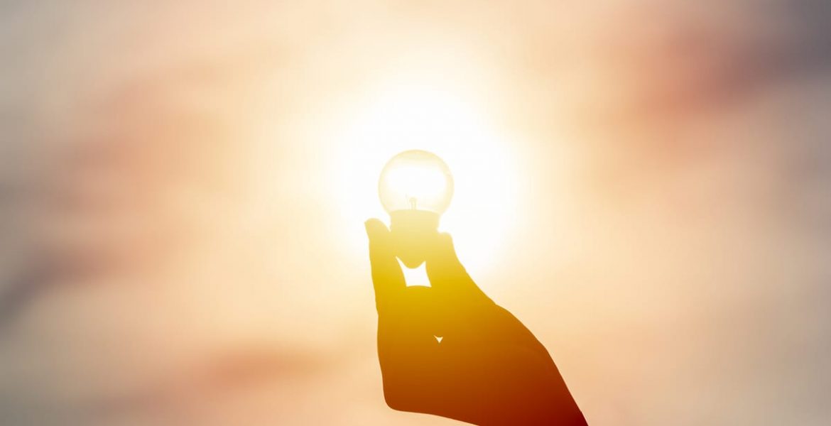 Mano sostiene una bombilla iluminada por el sol, símbolo de energía solar y sostenibilidad.