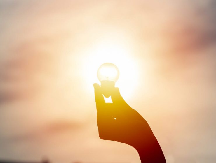 Mano sostiene una bombilla iluminada por el sol, símbolo de energía solar y sostenibilidad.