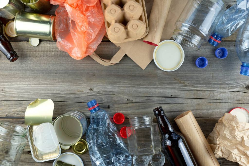 Diferentes tipos de residuos reciclables como plástico, vidrio, metal y papel, esparcidos sobre una mesa de madera, listos para ser clasificados.