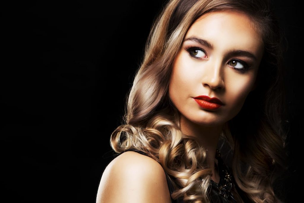 Maquillaje natural con labios rojos suaves y mirada iluminada en fondo oscuro