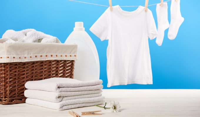 Ropa blanca colgada para secar junto a toallas dobladas y detergente para lavado.