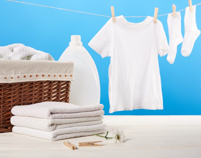 Ropa blanca colgada para secar junto a toallas dobladas y detergente para lavado.