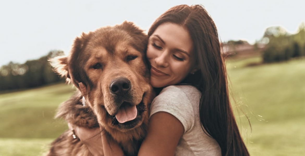 Mujer joven abrazando con cariño a un perro grande de pelaje marrón en un campo verde.