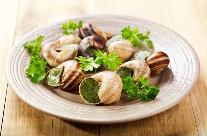 Caracoles servidos con mantequilla de ajo y perejil, listos para comer.