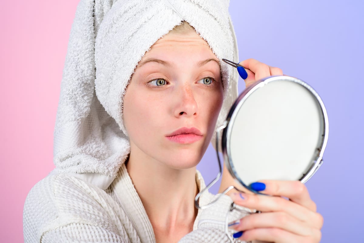 Mujer depilando sus cejas con pinzas, un paso clave en el tutorial de cómo maquillar las cejas para lograr una forma perfecta.