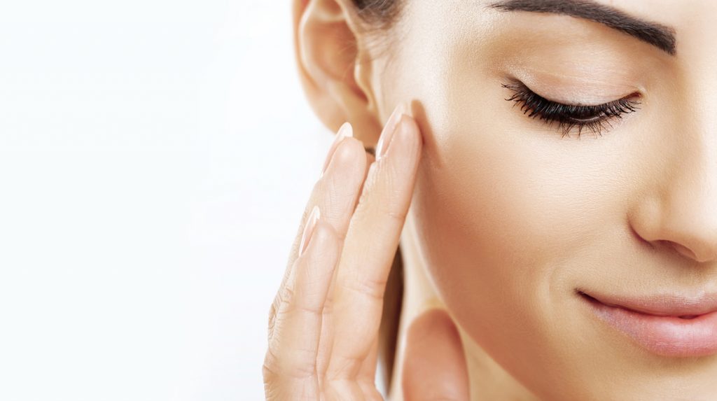 Mujer tocándose suavemente la mejilla con la yema de los dedos en rutina de skincare