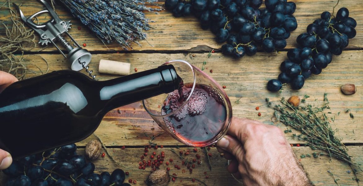 Copa de vino tinto servida con uvas frescas y hierbas sobre mesa rústica