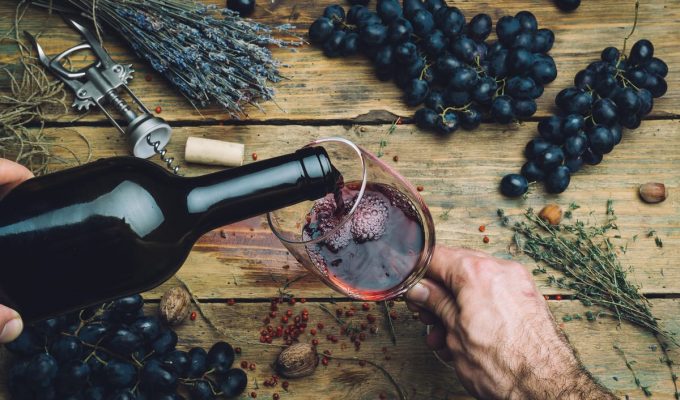 Copa de vino tinto servida con uvas frescas y hierbas sobre mesa rústica
